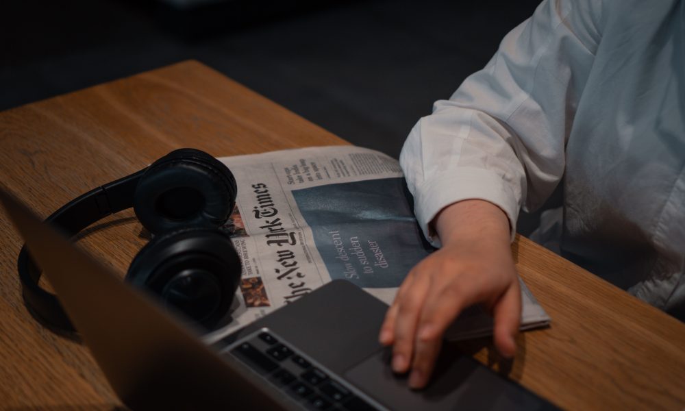 Hand on laptop with newspaper and headphones near