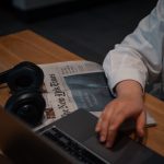 Hand on laptop with newspaper and headphones near