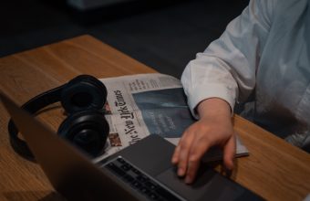 Hand on laptop with newspaper and headphones near